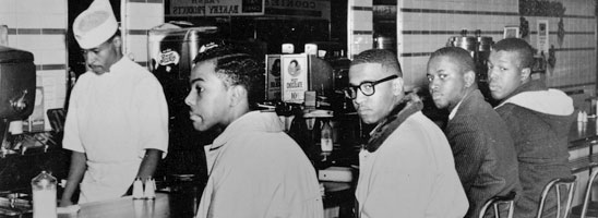 The Greensboro Four sit at a Woolworth’s lunch counter on February 1, 1960, as a Woolworth’s employee works behind the counter. 